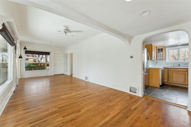 unfurnished living room with arched walkways, plenty of natural light, visible vents, and hardwood / wood-style floors