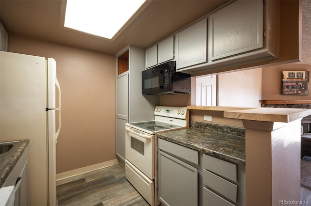 kitchen with dark hardwood / wood-style flooring, white refrigerator, kitchen peninsula, dark stone countertops, and stove