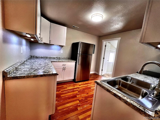 kitchen with a textured ceiling, freestanding refrigerator, dark wood-type flooring, visible vents, and a sink