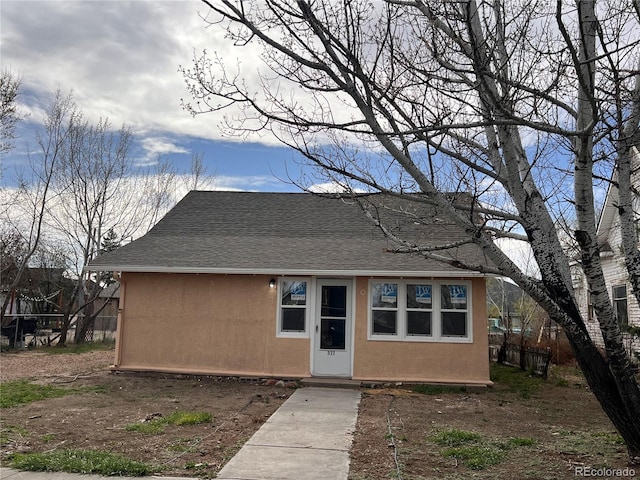 bungalow-style home with a shingled roof, stucco siding, and fence