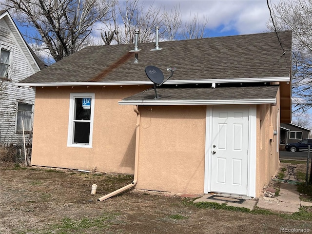 back of house featuring stucco siding and a shingled roof