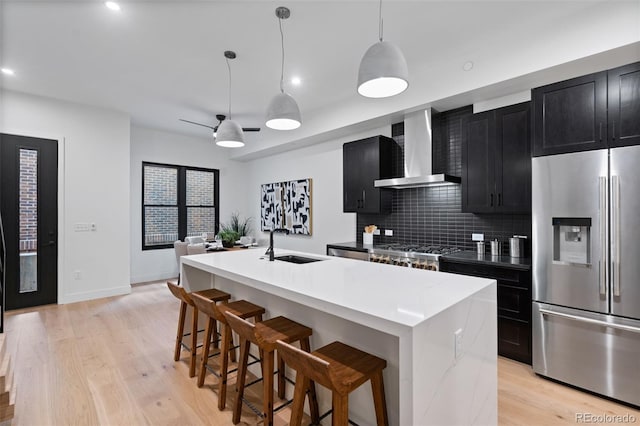 kitchen with stainless steel fridge with ice dispenser, sink, wall chimney exhaust hood, and a center island with sink