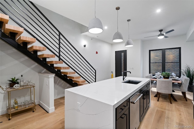 kitchen featuring pendant lighting, sink, light hardwood / wood-style flooring, a kitchen island with sink, and light stone countertops