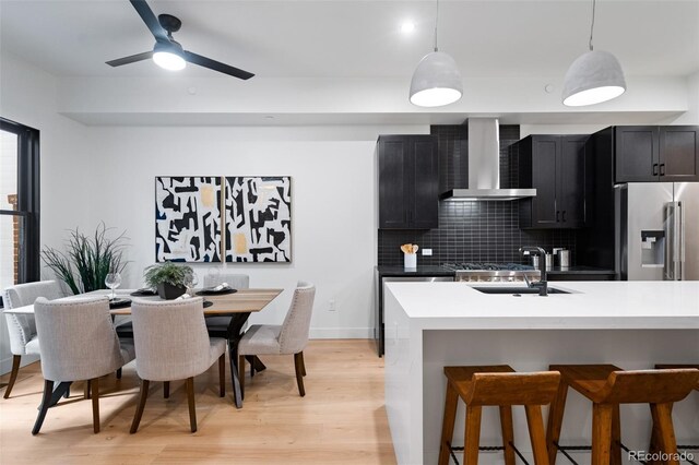 kitchen featuring wall chimney exhaust hood, decorative light fixtures, light wood-type flooring, high quality fridge, and decorative backsplash