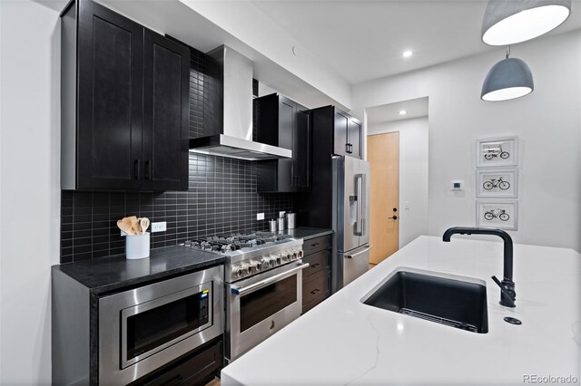 kitchen with wall chimney range hood, sink, tasteful backsplash, premium appliances, and decorative light fixtures