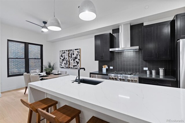 kitchen with decorative light fixtures, light stone countertops, sink, and wall chimney range hood