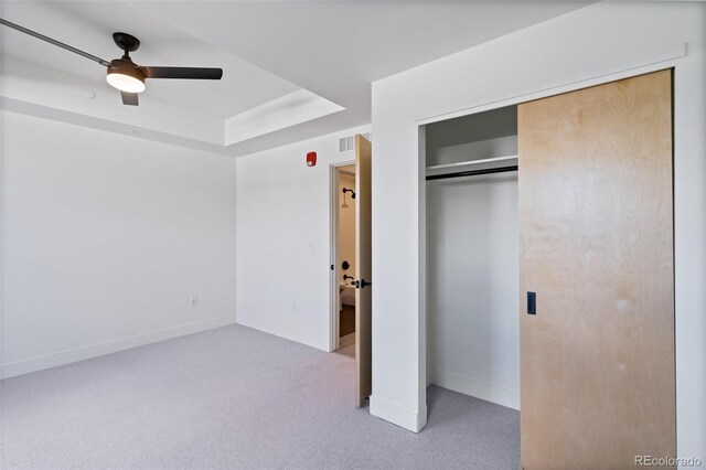 unfurnished bedroom with light carpet, a closet, a raised ceiling, and ceiling fan