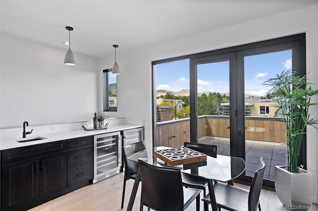 kitchen featuring sink, light hardwood / wood-style flooring, hanging light fixtures, wine cooler, and french doors