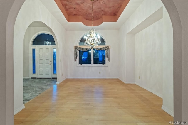 265 Ox Yoke Way, Monument, CO 80132 - unfurnished dining area with a chandelier, a raised ceiling, wood finished floors, arched walkways, and baseboards
