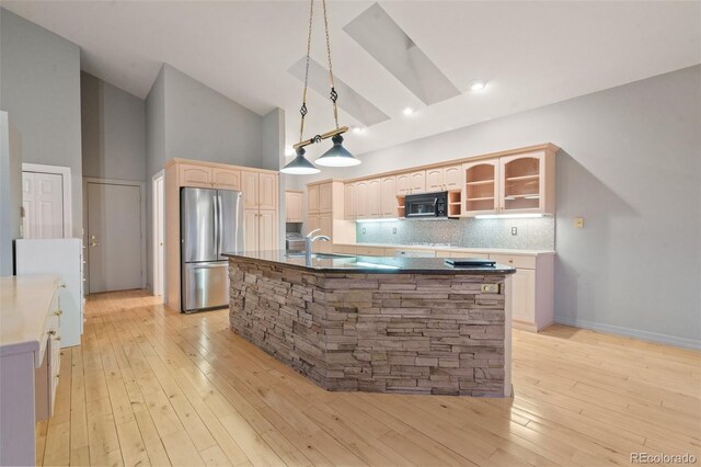 265 Ox Yoke Way, Monument, CO 80132 - kitchen featuring freestanding refrigerator, black microwave, high vaulted ceiling, a kitchen island with sink, and backsplash
