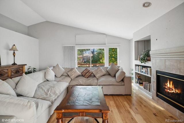 living room with light hardwood / wood-style floors, lofted ceiling, and a tile fireplace