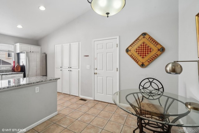 kitchen featuring light stone countertops, white cabinetry, vaulted ceiling, stainless steel refrigerator, and light tile patterned floors