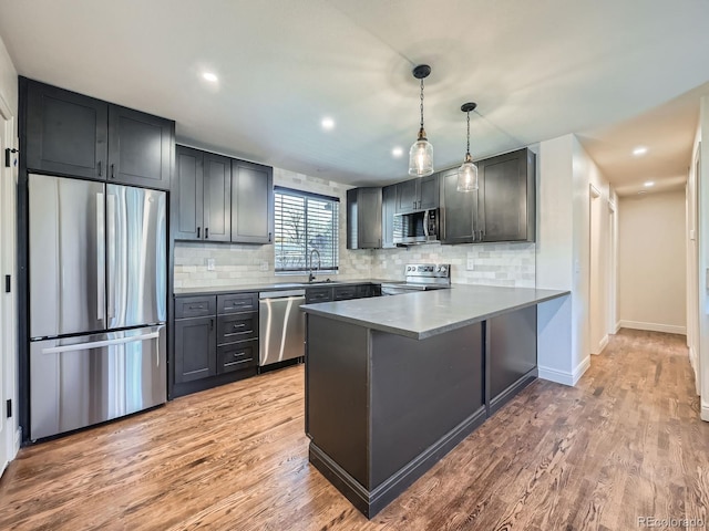 kitchen featuring hanging light fixtures, backsplash, kitchen peninsula, appliances with stainless steel finishes, and light wood-type flooring