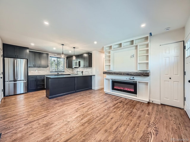 kitchen with decorative light fixtures, decorative backsplash, light wood-type flooring, and stainless steel appliances