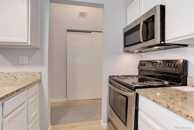 kitchen featuring visible vents, appliances with stainless steel finishes, light stone counters, light wood-style floors, and white cabinetry