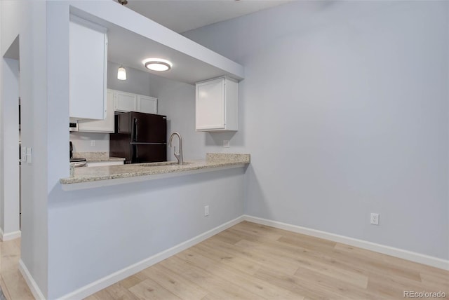 kitchen featuring baseboards, freestanding refrigerator, light wood-style floors, white cabinetry, and a sink