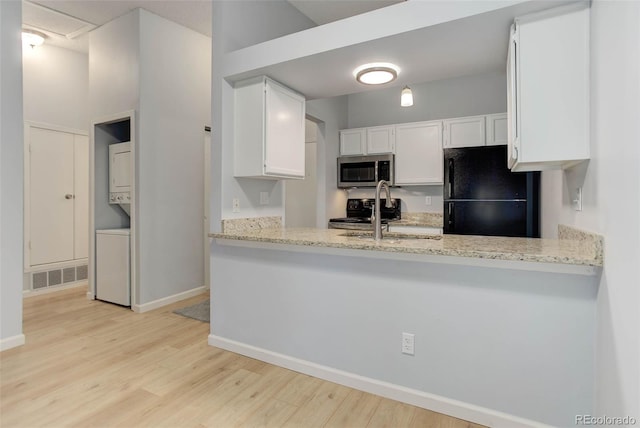 kitchen featuring stacked washer and clothes dryer, stainless steel microwave, visible vents, freestanding refrigerator, and a sink