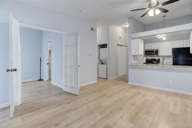 kitchen with stacked washer and dryer, electric range, visible vents, stainless steel microwave, and freestanding refrigerator