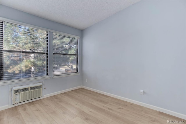 spare room with a textured ceiling, a wall unit AC, wood finished floors, and baseboards