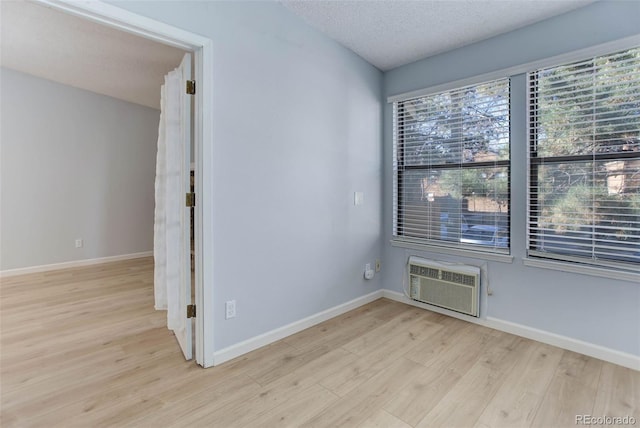 spare room featuring a textured ceiling, baseboards, wood finished floors, and a wall mounted air conditioner