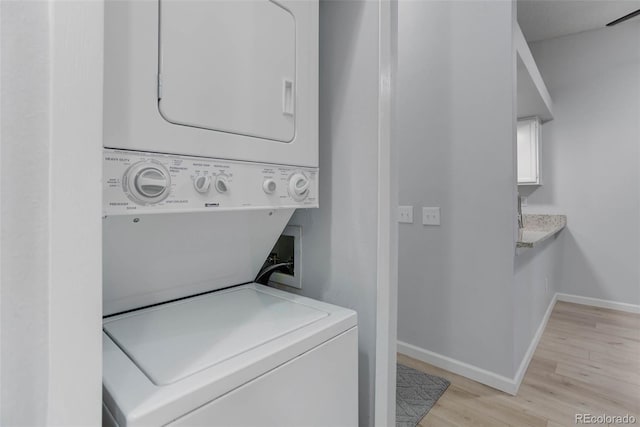 laundry room featuring laundry area, stacked washer / dryer, light wood-type flooring, and baseboards