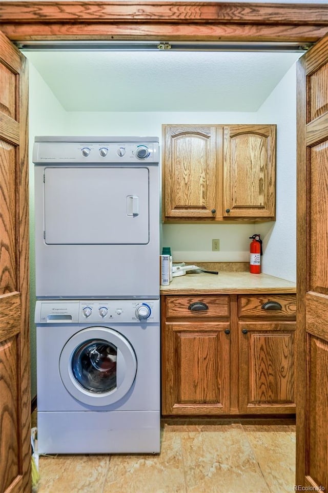 laundry area featuring stacked washer and clothes dryer, cabinets, and light tile flooring