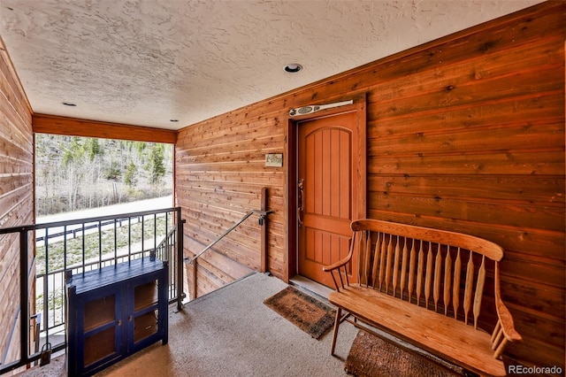 interior space with a textured ceiling, carpet floors, multiple windows, and wood walls