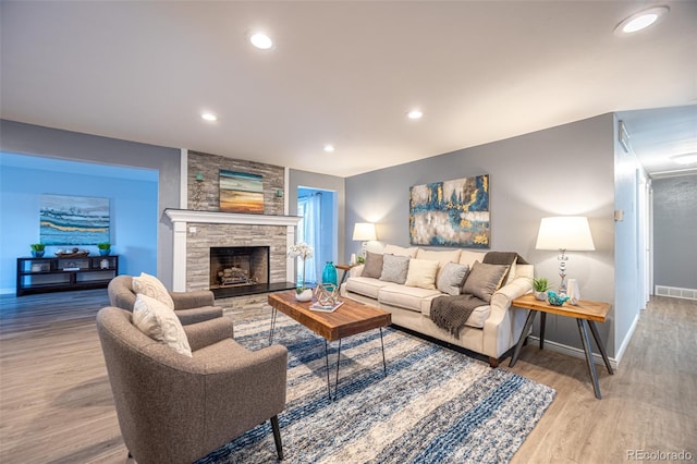 living room with visible vents, baseboards, a stone fireplace, recessed lighting, and wood finished floors