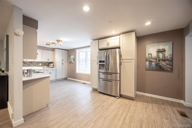 kitchen featuring light wood-type flooring, visible vents, stainless steel refrigerator with ice dispenser, light countertops, and decorative backsplash