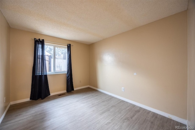 unfurnished room with visible vents, a textured ceiling, baseboards, and wood finished floors