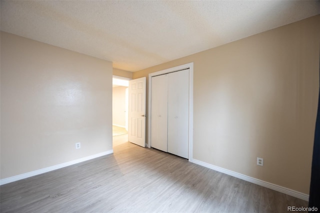 unfurnished bedroom featuring a closet, baseboards, a textured ceiling, and wood finished floors