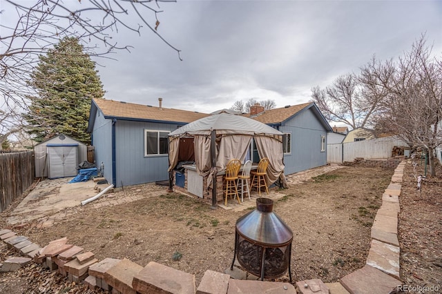 back of house with an outbuilding, a storage shed, a fire pit, and a fenced backyard