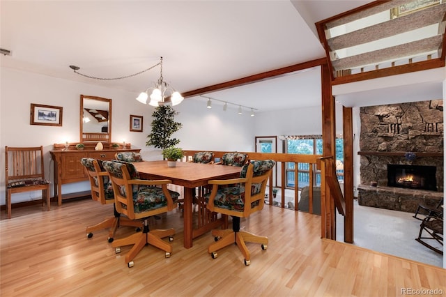 dining space with beam ceiling, a chandelier, light wood finished floors, and a stone fireplace