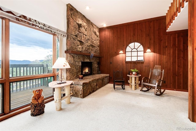 sitting room with a stone fireplace, carpet flooring, a mountain view, and wood walls