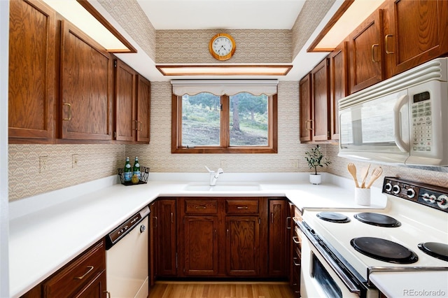 kitchen with white appliances, light countertops, light wood finished floors, and a sink