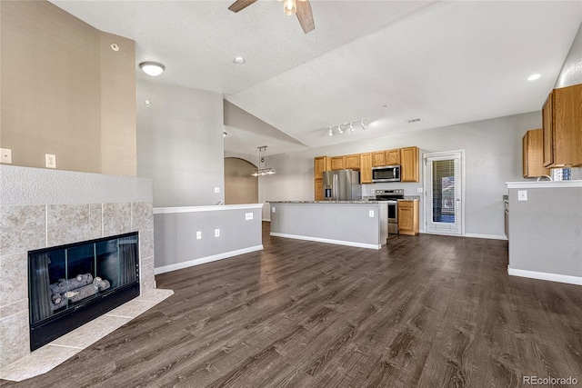 unfurnished living room featuring ceiling fan, dark wood-type flooring, a textured ceiling, vaulted ceiling, and a tiled fireplace