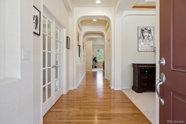 hallway featuring recessed lighting, arched walkways, baseboards, and light wood-type flooring