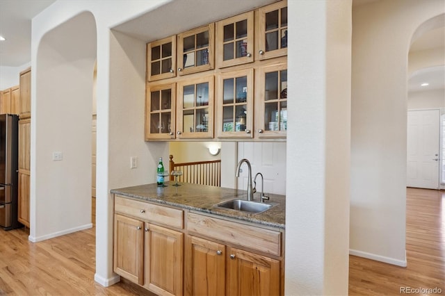bar with arched walkways, a sink, baseboards, freestanding refrigerator, and light wood-style flooring