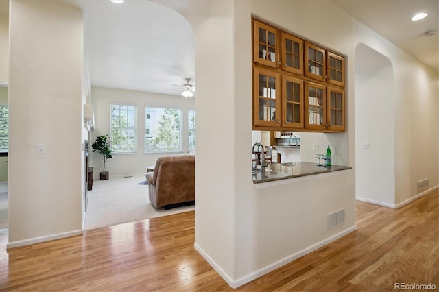 hall with arched walkways, baseboards, light wood-style flooring, and visible vents