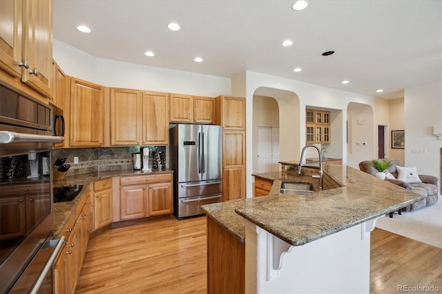 kitchen with appliances with stainless steel finishes, arched walkways, light wood-style floors, a breakfast bar, and recessed lighting