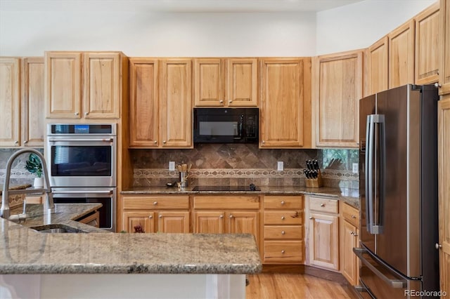 kitchen featuring light brown cabinets, light stone countertops, light wood-style flooring, backsplash, and black appliances