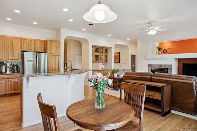 dining area with ceiling fan, light wood-style floors, arched walkways, a tiled fireplace, and recessed lighting