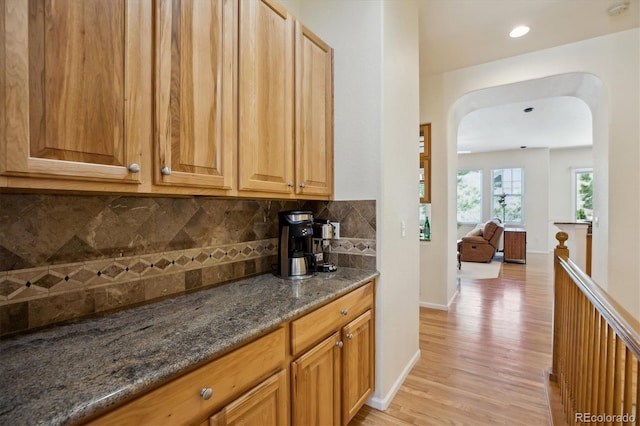 interior space featuring decorative backsplash, baseboards, light wood-type flooring, arched walkways, and dark stone countertops