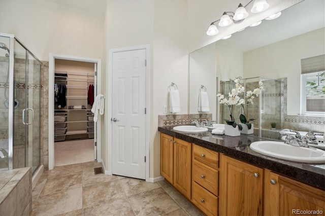 full bathroom with double vanity, a spacious closet, a shower stall, and a sink