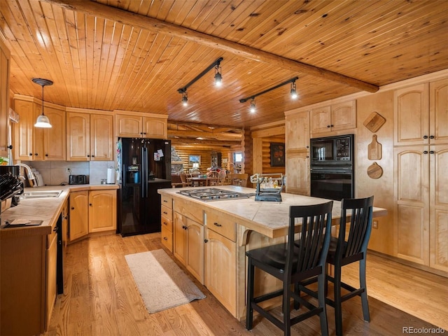 kitchen featuring a sink, light brown cabinetry, a center island, light wood-type flooring, and black appliances