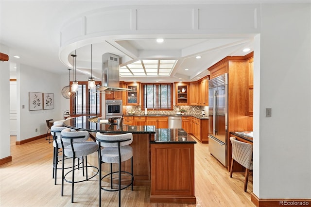 1351 S Milwaukee St, Denver, CO 80210 - kitchen with stainless steel appliances, brown cabinetry, island range hood, light wood-style floors, and recessed lighting