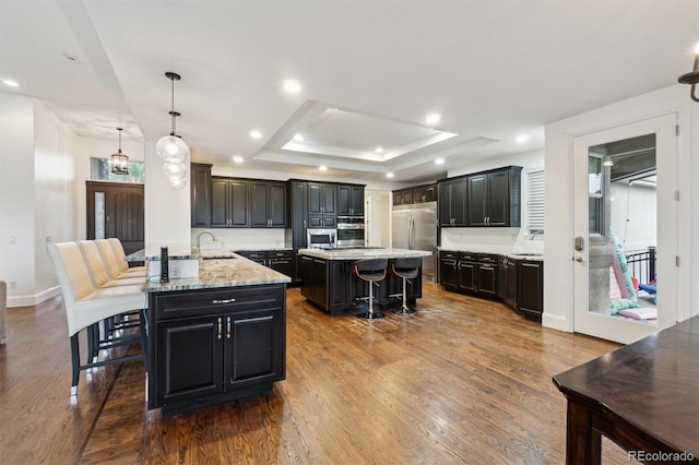 12939 Wabash Ct, Thornton, CO 80602 - kitchen with stainless steel appliances, a kitchen island, a breakfast bar area, dark wood-style floors, and a raised ceiling