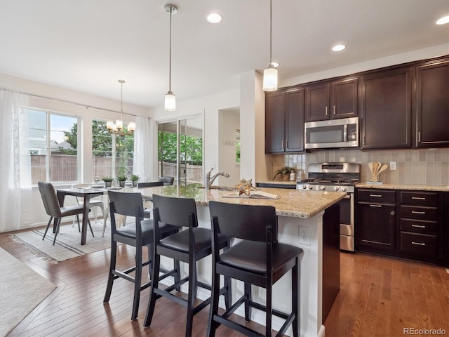 15350 W 50th Dr, Golden, CO 80403 - kitchen featuring stainless steel appliances, tasteful backsplash, light stone countertops, a kitchen island with sink, and wood-type flooring