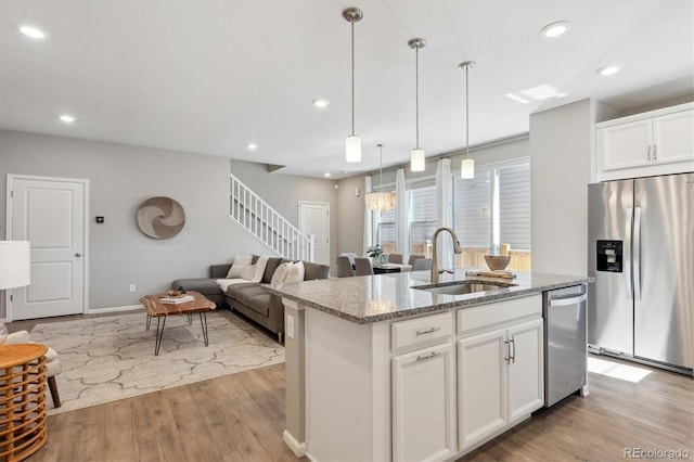 kitchen with light wood finished floors, appliances with stainless steel finishes, a sink, an island with sink, and light stone countertops