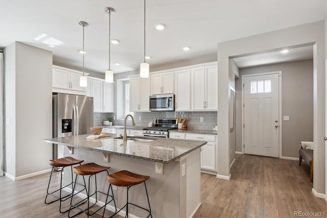 kitchen featuring decorative backsplash, stainless steel appliances, a kitchen bar, white cabinetry, and a sink